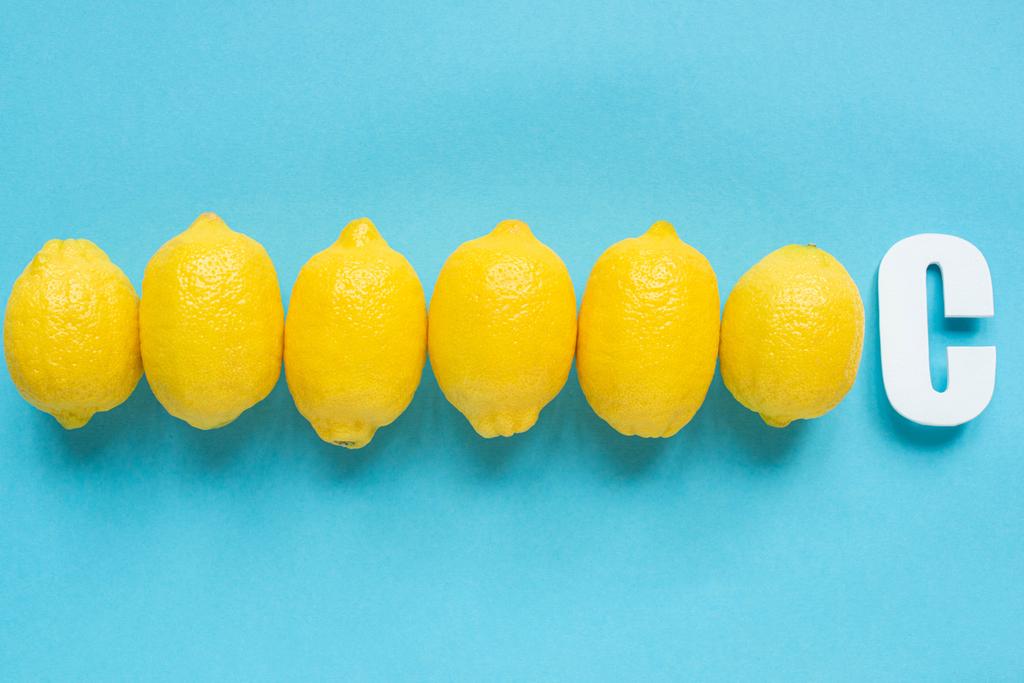 Draufsicht auf reife gelbe Zitronen und Buchstabe C auf blauem Hintergrund - Foto, Bild