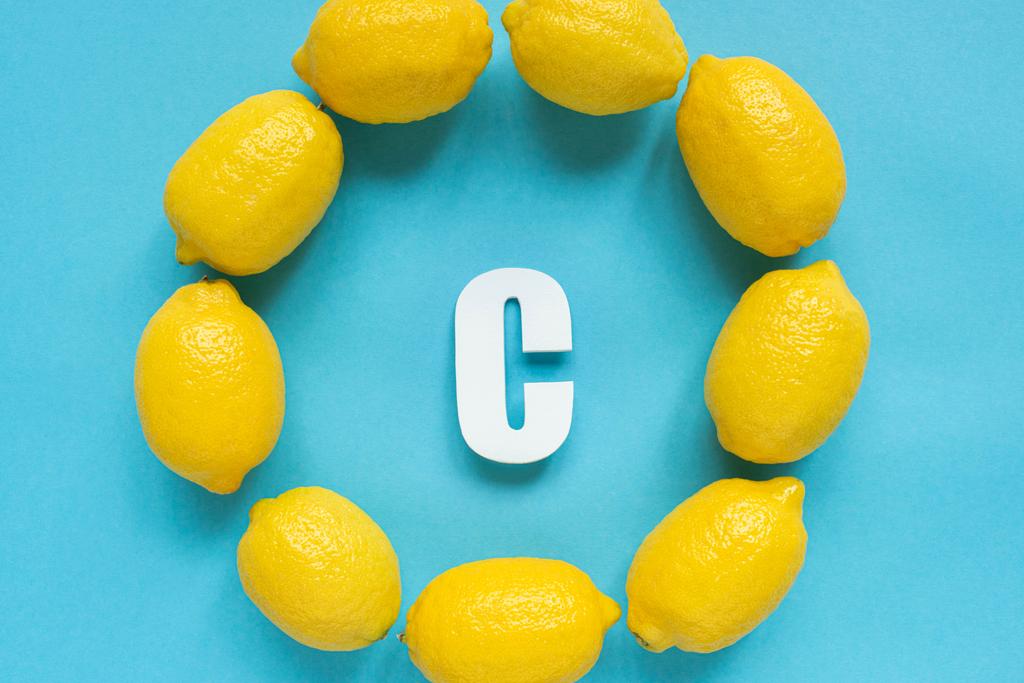 πάνω όψη ώριμων κίτρινων λεμονιών γύρω από το γράμμα C σε μπλε φόντο - Φωτογραφία, εικόνα