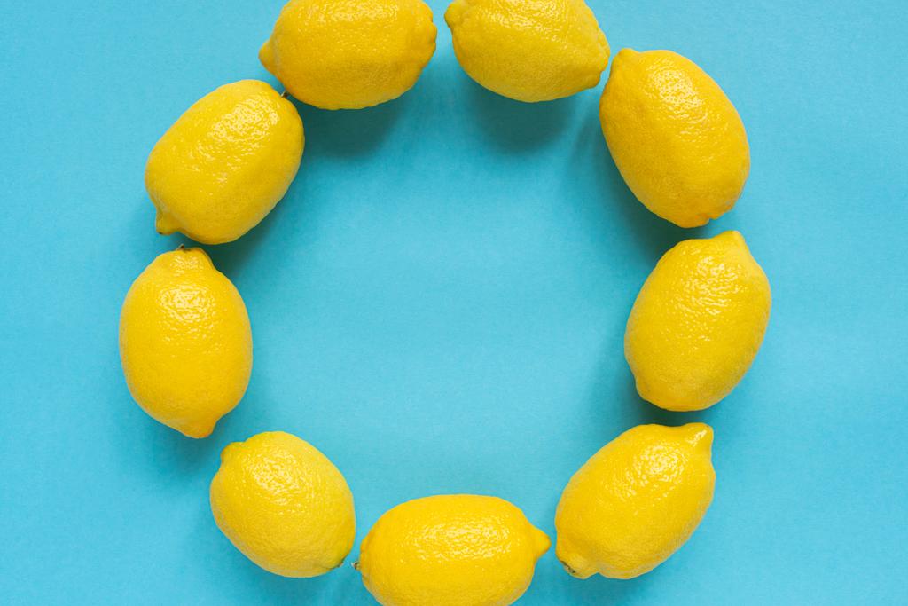 верхний вид спелых желтых лимонов, расположенных в круглой пустой рамке на синем фоне
 - Фото, изображение
