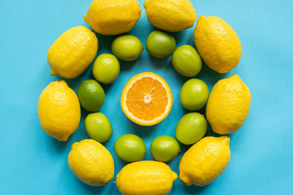 top view of ripe yellow lemons, orange and limes arranged in circles on blue background - Photo, Image