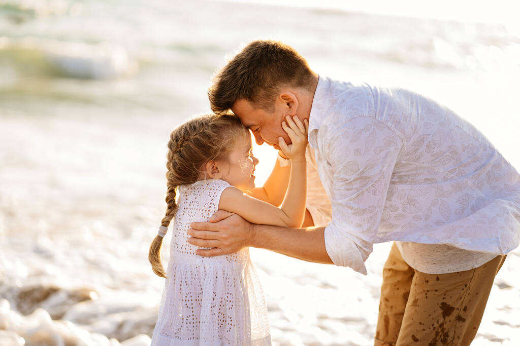 Csók. Apa a lányával a tengerparton sétál szeles időben. szórakoztató család. - Fotó, kép