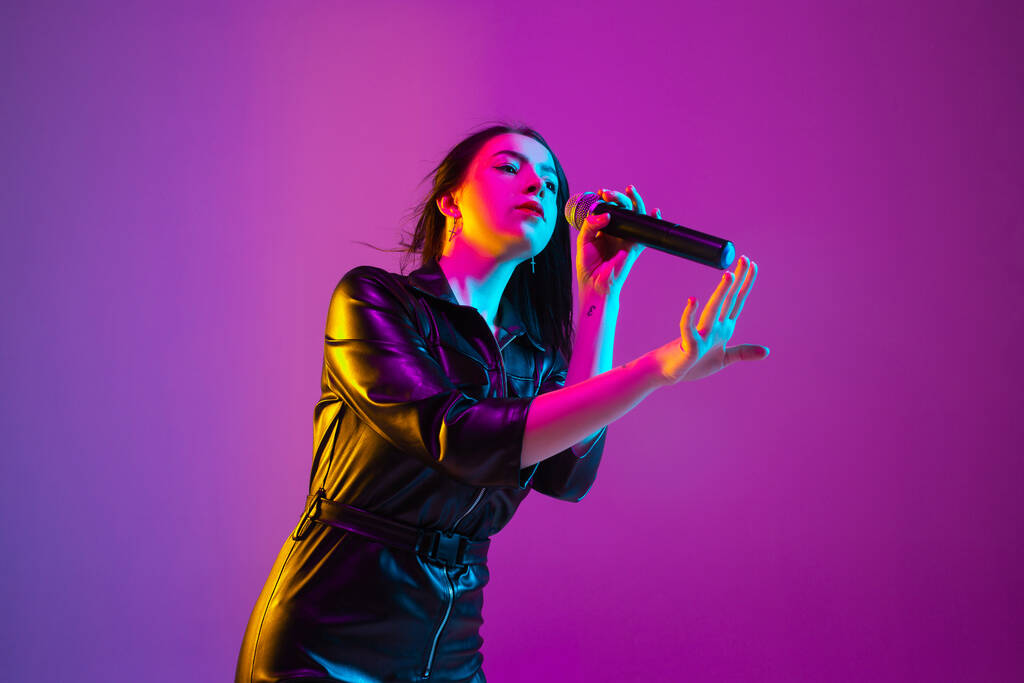 Кавказький жіночий портрет співачки ізольований на пурпуровому фоні студії в неоновому світлі - Фото, зображення