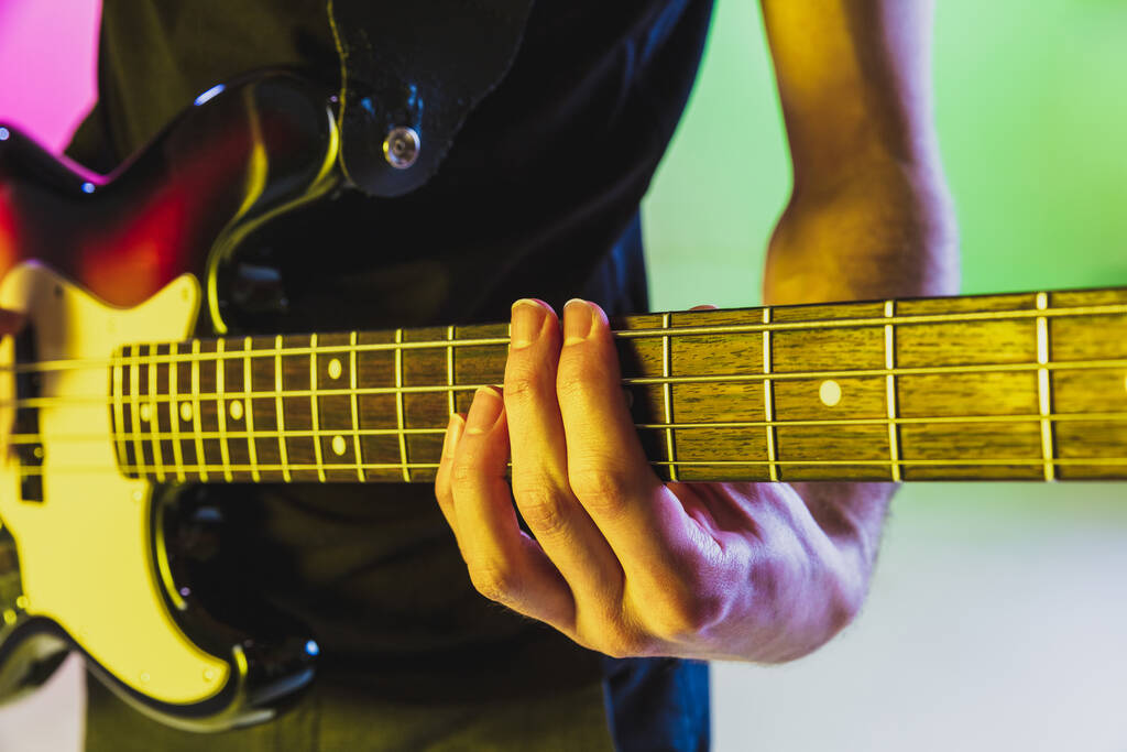 Zamknij ręce muzyk gra na gitarze basowej na gradientowym tle studio w świetle neonu - Zdjęcie, obraz