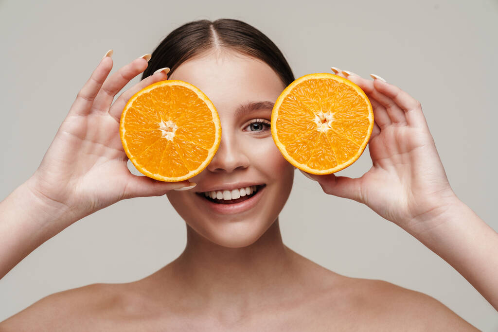Зображення веселої милої без сорочки, посміхаючись, позуючи з апельсином ізольовано на сірому фоні
 - Фото, зображення