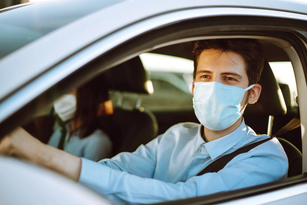 Nuori mies steriilissä lääketieteellisessä naamiossa istuu autossa epidemian aikana karanteenikaupungissa. Terveyden suojelu, turvallisuus ja pandemia. Viileä - 19. - Valokuva, kuva