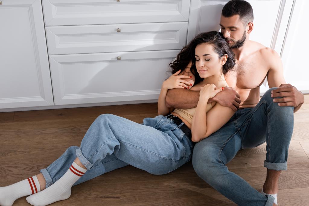 Мускулистый мужчина обнимает красивую девушку, сидя на полу
  - Фото, изображение