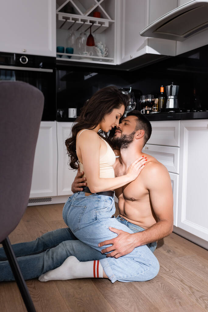sexy jonge vrouw zitten op shirtless man in keuken  - Foto, afbeelding