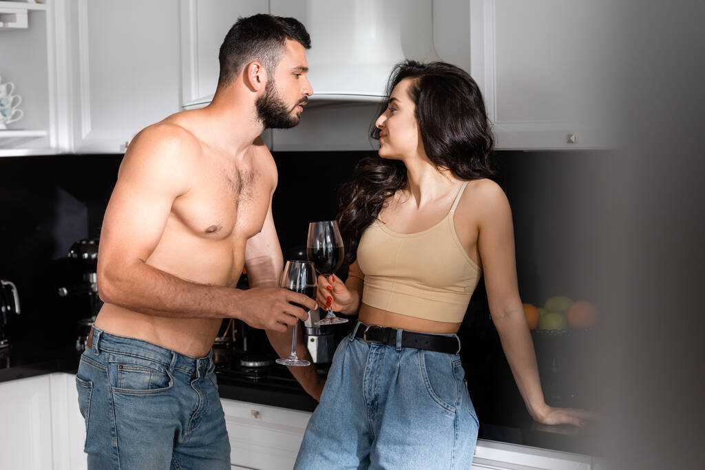 enfoque selectivo de hombre sin camisa y mujer feliz sosteniendo vasos de vino tinto y mirándose el uno al otro
 - Foto, imagen