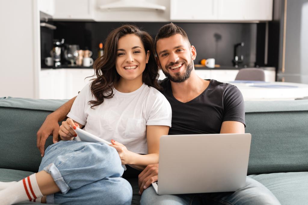 šťastný mladý pár dívá na kameru a drží gadgets  - Fotografie, Obrázek
