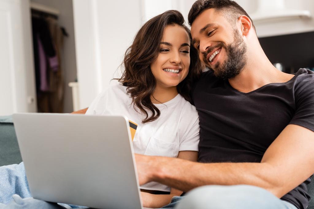 happy woman holding credit card near bearded boyfriend and laptop  - Photo, Image