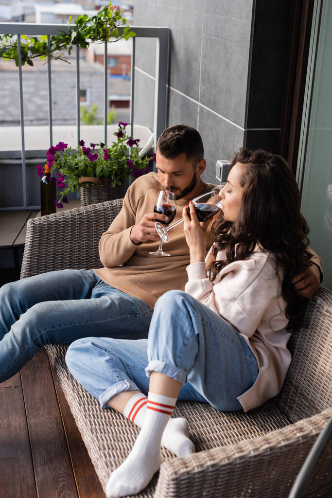 schöner Mann und attraktive Frau sitzen auf dem Sofa im Freien und trinken Rotwein - Foto, Bild
