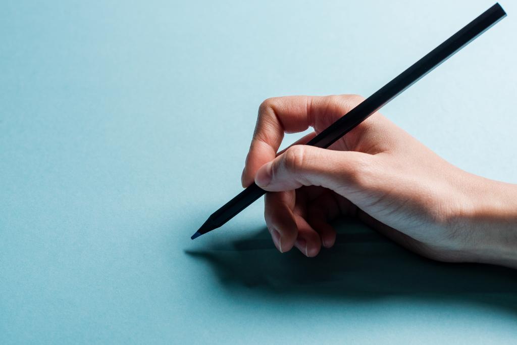 Обрізаний вид дизайнера, що тримає олівець на синій поверхні
 - Фото, зображення
