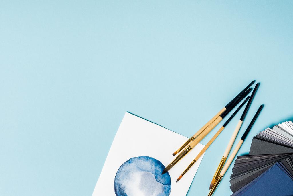 Vista dall'alto di pennelli su pittura ad acquerello e campioni di colore su sfondo blu
 - Foto, immagini