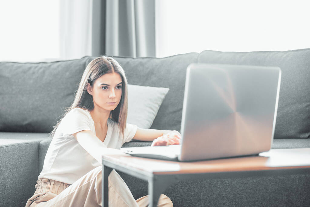 Fiatal nő modern laptoppal otthon ül a kanapén. Boldog lány böngészi az interneten a szabadidő alatt..  - Fotó, kép