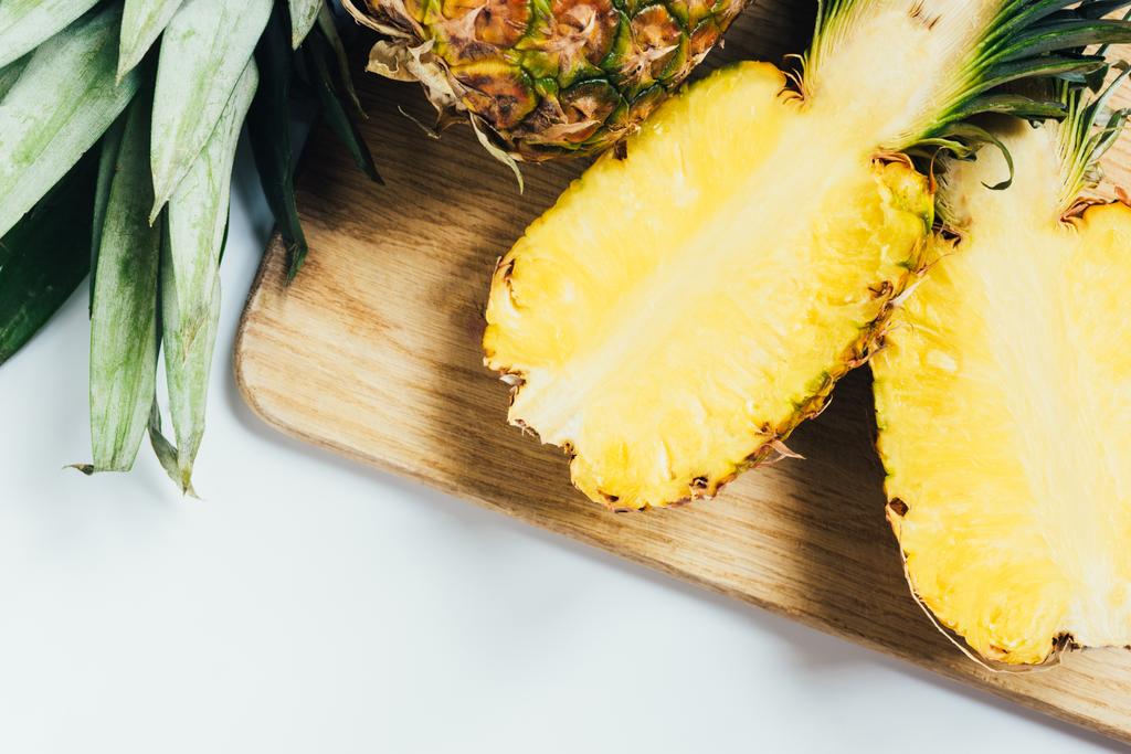 Draufsicht auf saftige Ananashälften auf Holzschneidebrett auf weißem Hintergrund - Foto, Bild