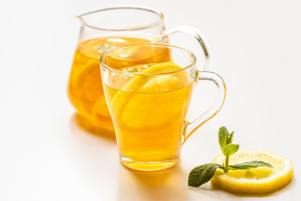 selectieve focus van hete thee in glas en theepot in de buurt van citroen en munt op witte achtergrond - Foto, afbeelding