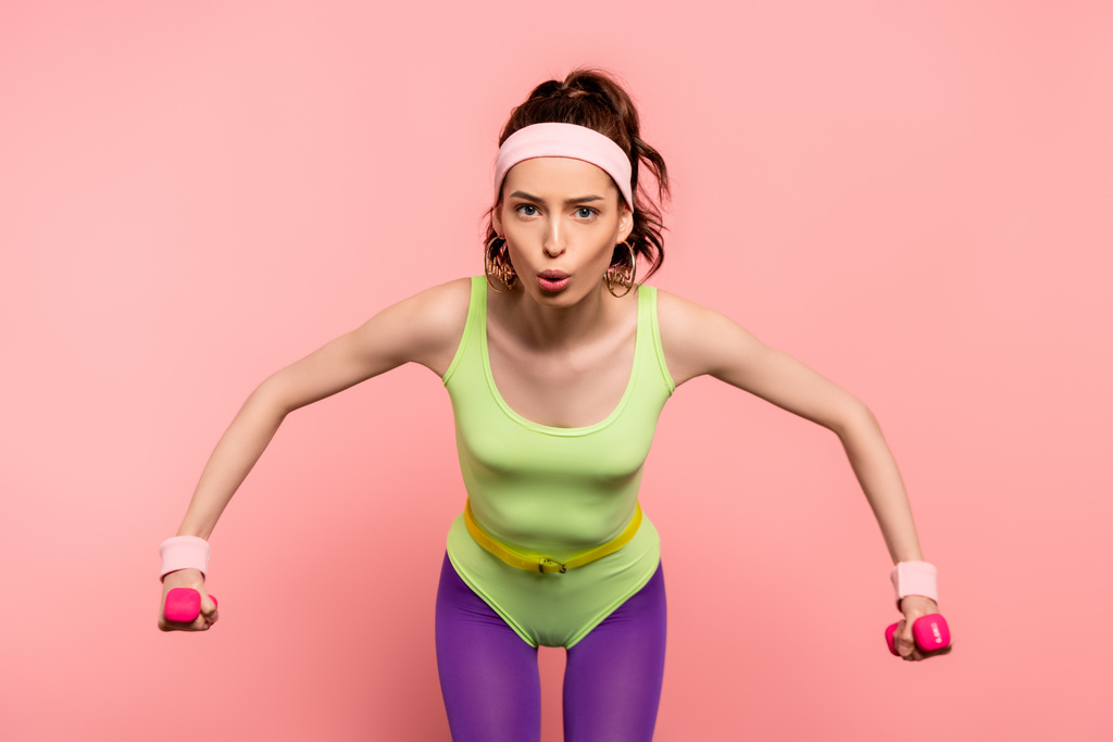 emotional sportswoman exercising with dumbbells isolated on pink  - Photo, Image