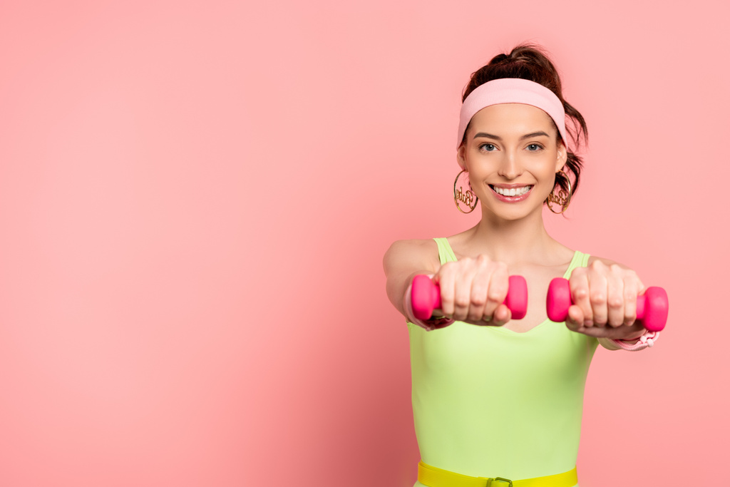 счастливая спортсменка упражняется с гантелями на розовый
  - Фото, изображение