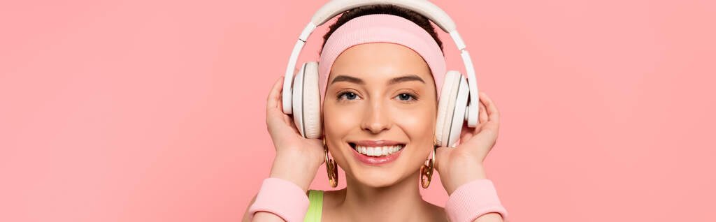 ピンクに隔離された音楽を聴きながらヘッドフォンに触れる陽気な女の子の水平イメージ  - 写真・画像