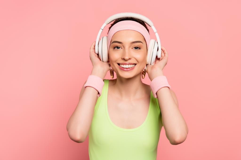 cheerful girl touching headphones while listening music isolated on pink  - Photo, Image
