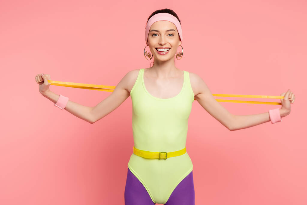 happy sportswoman exercising with resistance band on pink  - Photo, Image