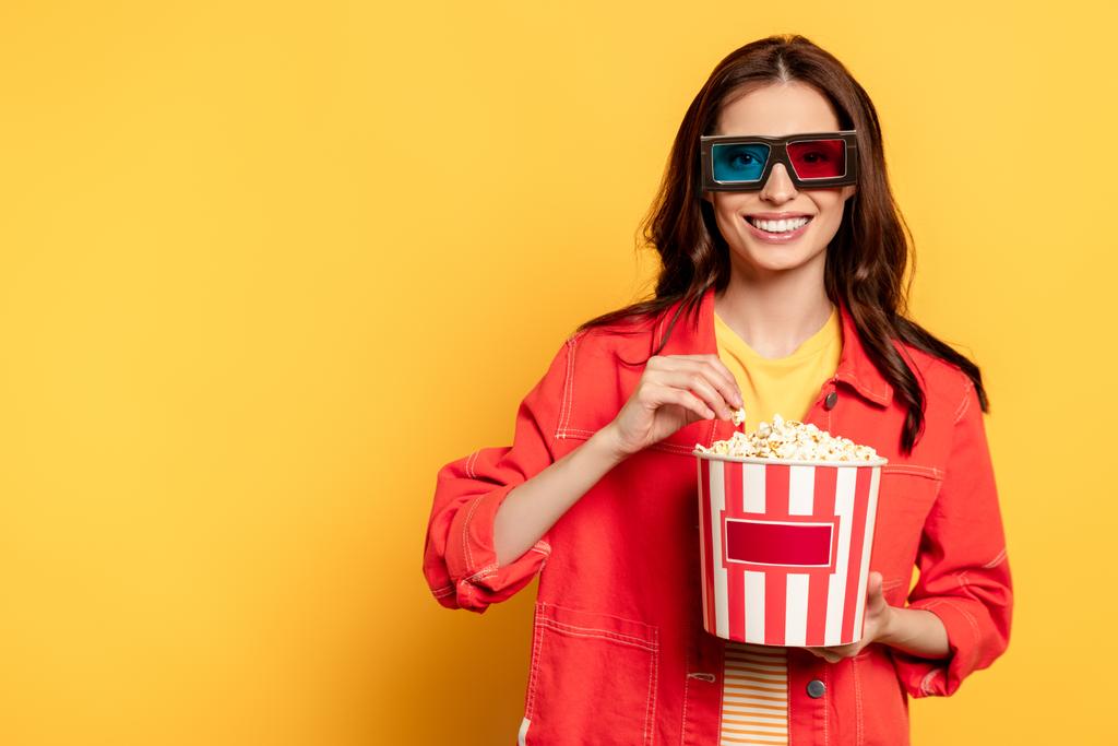 cheerful young woman in 3d glasses holding popcorn bucket on yellow - Photo, Image