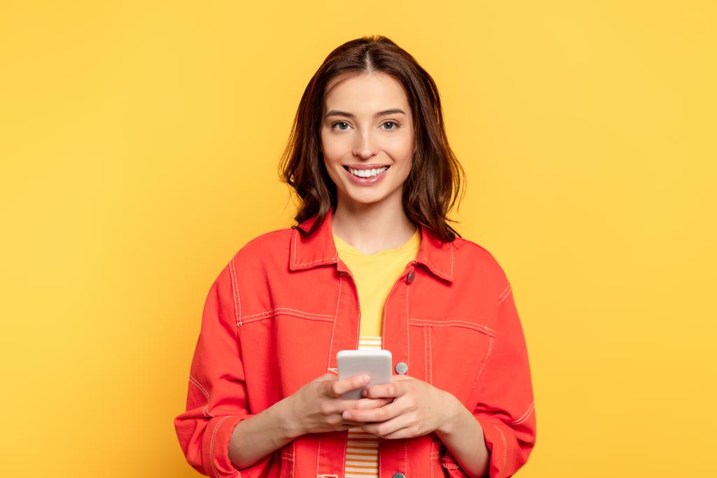heureuse jeune femme tenant smartphone isolé sur jaune  - Photo, image
