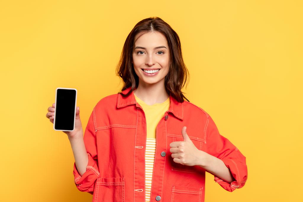 feliz joven sosteniendo teléfono inteligente con pantalla en blanco y mostrando el pulgar hacia arriba en amarillo
  - Foto, Imagen