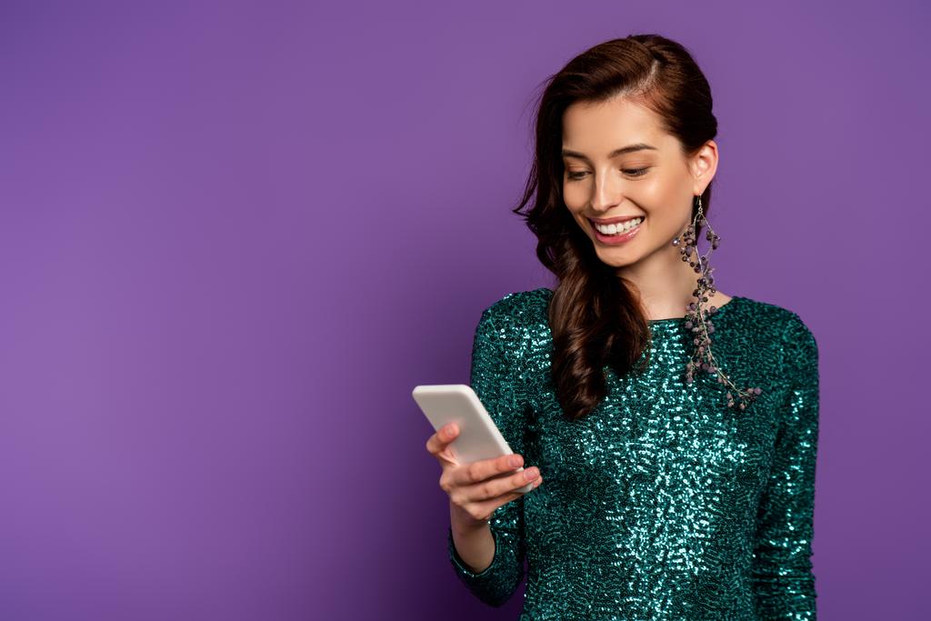 Ευτυχισμένη νεαρή γυναίκα κοιτάζοντας smartphone σε μωβ  - Φωτογραφία, εικόνα