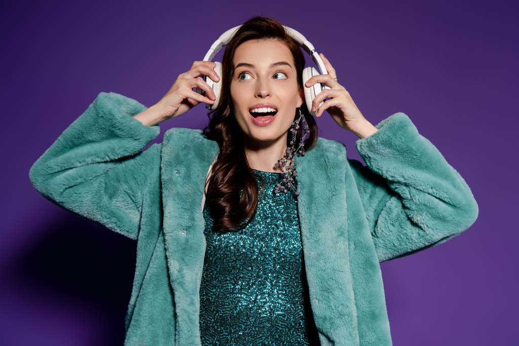 mujer emocionada tocando auriculares y mirando hacia otro lado en púrpura
  - Foto, Imagen