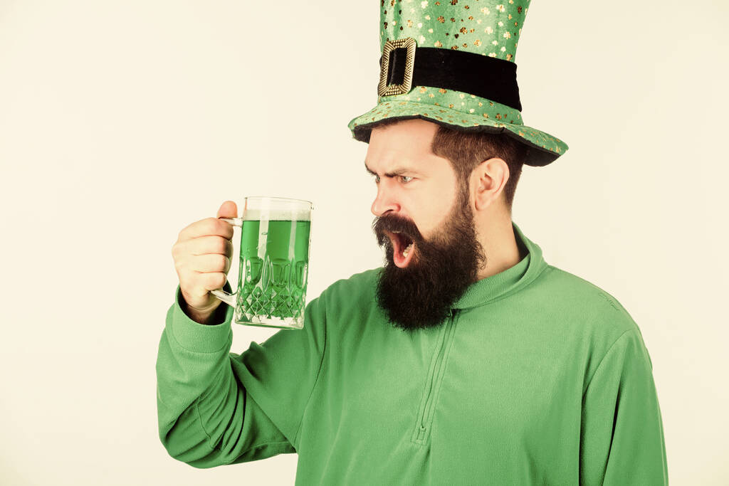 Irlandczyk, dopóki nie zemdleję. Hipster w karłowatym kapeluszu trzymający kubek z piwem. Irlandczyk z brodą pijący zielone piwo. Człowiek z brodą wznoszący toast za dzień świętych Patricków. Świętowanie dnia świętych Patricków w barze - Zdjęcie, obraz