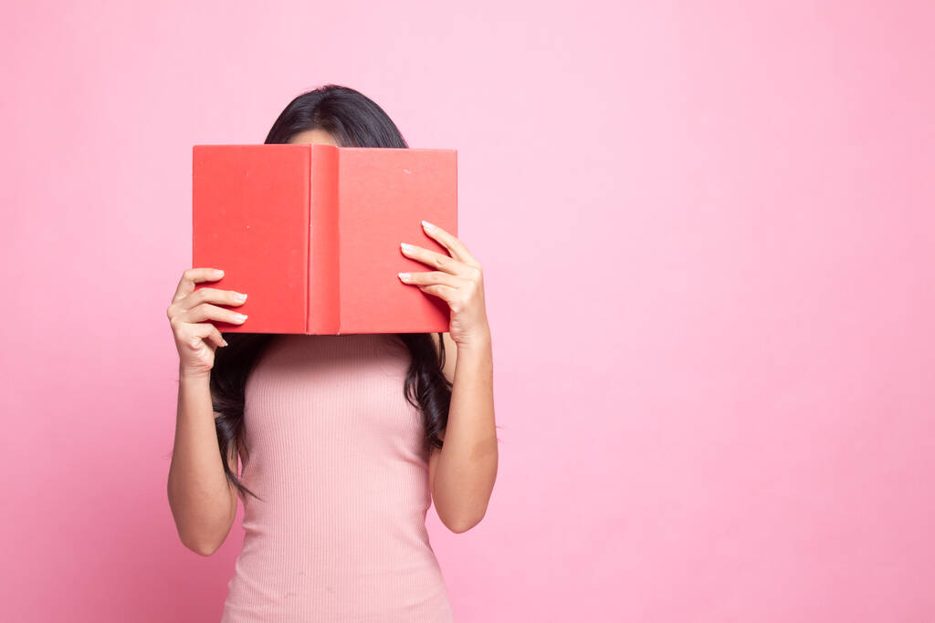 Jeune femme asiatique avec une couverture de livre son visage sur fond rose
 - Photo, image