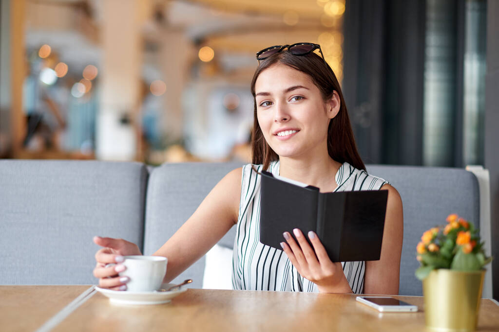 Mujer joven en un café leyendo un libro electrónico y tomando café. - Foto, imagen