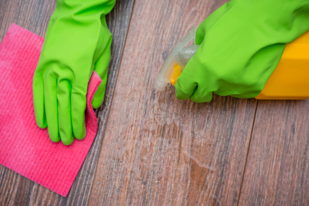 Elleri lastik eldivenli, elinde bir sprey ve ıslak temizleme bezi tutan eller. Binanın dezenfekte edilmesi, viral ve bakteriyel hastalıkların önlenmesi. Ahşap yüzeylerin temizlenmesi. - Fotoğraf, Görsel