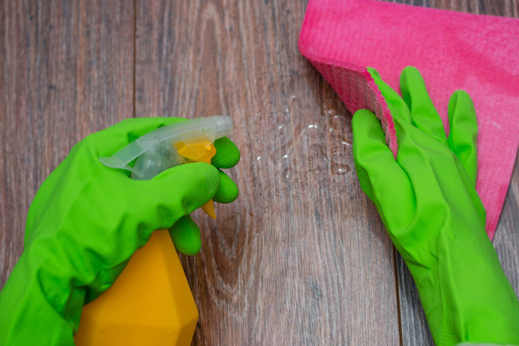 Close-up van de handen in rubberen handschoenen met een spuitfles en vodden voor natte reiniging. Concept van desinfectie van gebouwen, preventie van virale en bacteriële ziekten. Reiniging van houten oppervlakken. - Foto, afbeelding