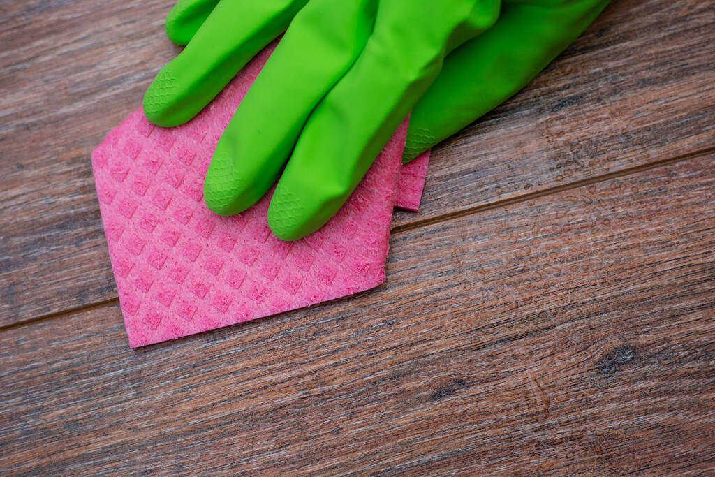 lähikuva kädestä vihreässä kumihanskassa hankaamassa märkää puupintaa. Tilojen desinfioinnin käsite, virus- ja bakteeritautien ehkäisy. Puupintojen puhdistus. - Valokuva, kuva