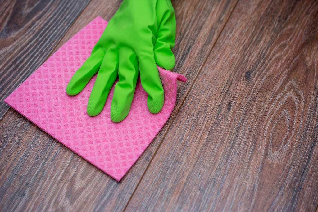 Крупный план руки в зеленой резиновой перчатке, потирая влажную деревянную поверхность. Концепция дезинфекции предпосылок, профилактики вирусных и бактериальных заболеваний. Очистка деревянных поверхностей
. - Фото, изображение