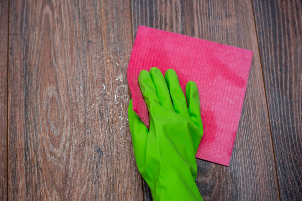 Primer plano de una mano en un guante de goma verde frotando una superficie de madera húmeda. El concepto de desinfección de locales, la prevención de enfermedades virales y bacterianas. Limpieza de superficies de madera
. - Foto, Imagen