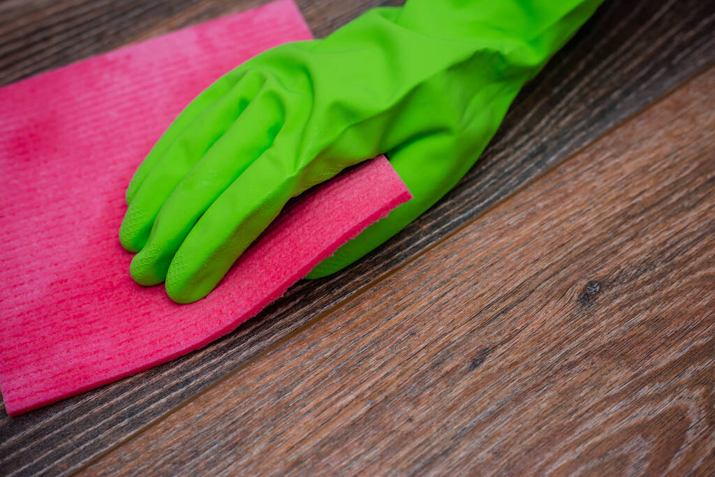 Крупним планом рука в зеленій гумовій рукавичці натирає вологу дерев'яну поверхню. Концепція дезінфекції приміщень, профілактика вірусних та бактеріальних захворювань. Очищення дерев'яних поверхонь
. - Фото, зображення