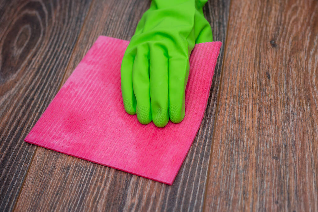 Primer plano de una mano en un guante de goma verde frotando una superficie de madera húmeda. El concepto de desinfección de locales, la prevención de enfermedades virales y bacterianas. Limpieza de superficies de madera
. - Foto, imagen