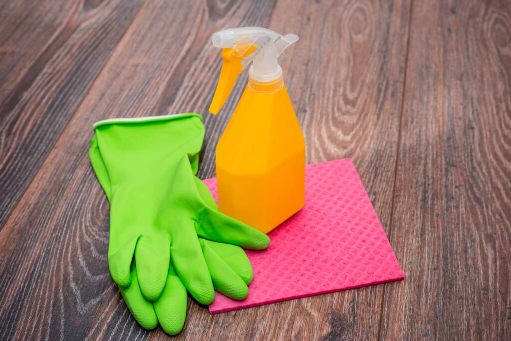 Közelkép egy spray palackról, gumikesztyűről és egy nedves rongyról a padlón. A helyiségek fertőtlenítésének koncepciója, a vírusos és bakteriális betegségek megelőzése. Fa felületek tisztítása. - Fotó, kép