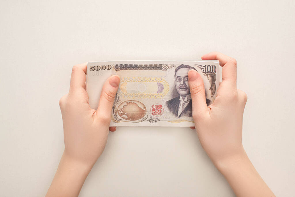 KYIV, UKRAINE - MÁRCIUS 25, 2020: levágott nézet egy japán jen bankjegyet tartó nőről fehér alapon - Fotó, kép