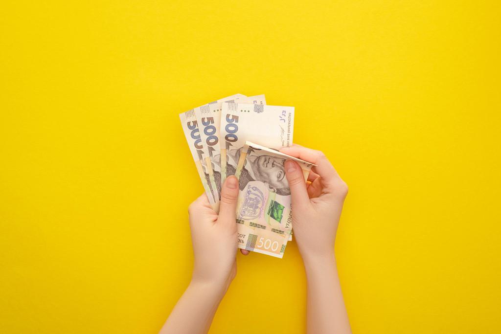 KIEW, UKRAINE - 25. MÄRZ 2020: Draufsicht einer Frau, die ukrainische Griwna-Banknoten isoliert auf gelb zählt  - Foto, Bild