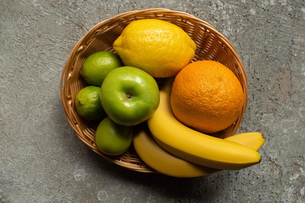 vista superior de coloridas frutas frescas en canasta de mimbre sobre superficie de hormigón gris
 - Foto, imagen
