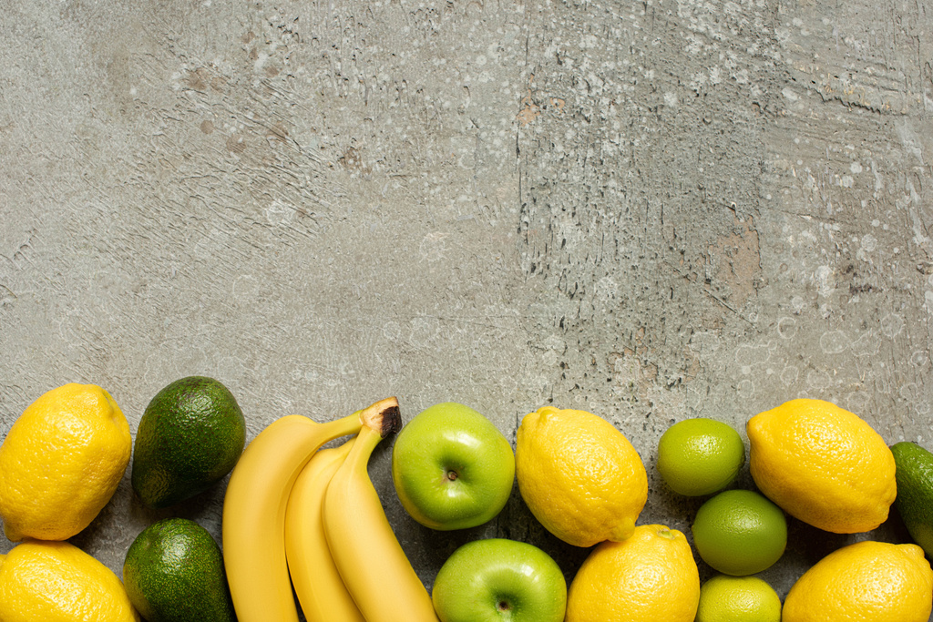 pohled na barevné banány, jablka, avokádo, citrony a citrony na šedém betonovém povrchu - Fotografie, Obrázek