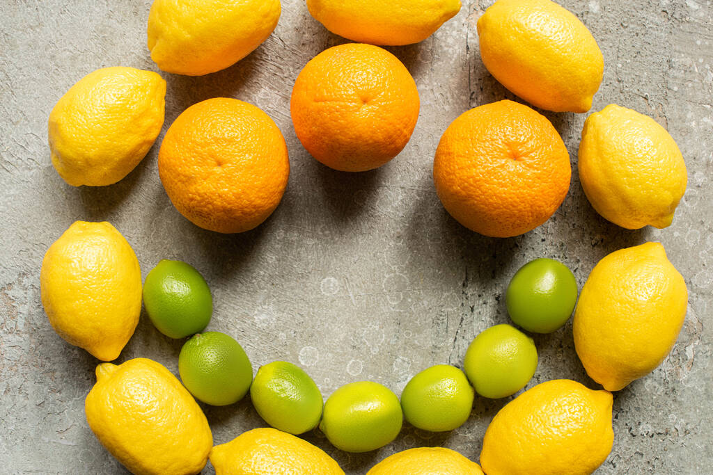 top view of colorful oranges, avocado, limes and lemons arranged in circle on grey concrete surface - Photo, Image