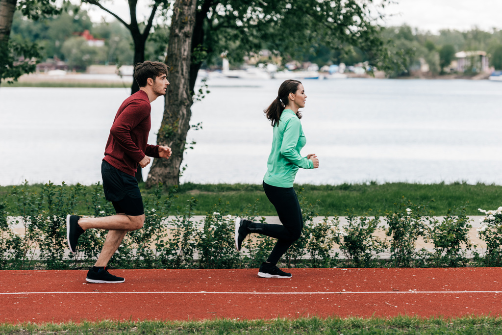 Boční pohled na pár běžící na běžecké trati v parku  - Fotografie, Obrázek