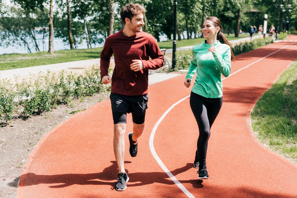 Sportswoman smiling at boyfriend while running on track in park  - Photo, Image