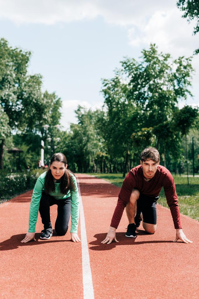 Young couple in starting position on running track in park - Photo, Image