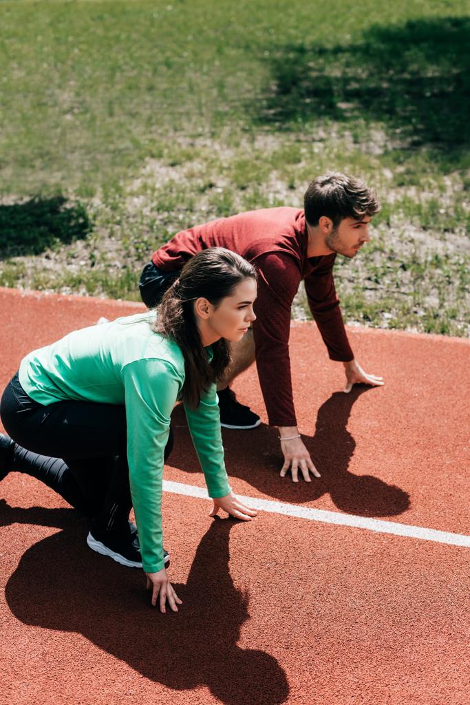 Side view of couple in sportswear standing in starting position on track in park  - Photo, Image
